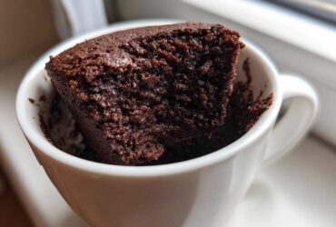 Close-up of a rich, dark chocolate Cottage Cheese Microwave Brownie sticking out of a white mug.