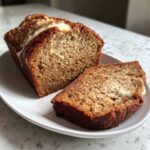 A loaf of cream cheese banana bread, partially sliced, showing the moist interior and cream cheese swirl.