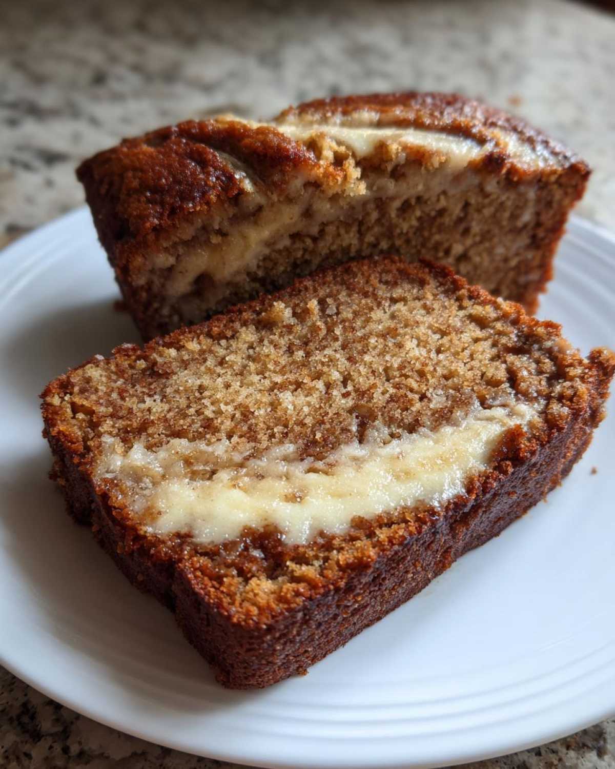 A close-up of two slices of moist cream cheese banana bread showing the rich brown color and creamy center swirl.