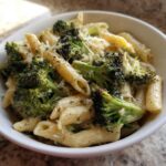 A close-up of creamy broccoli pasta featuring penne noodles, bright green broccoli florets, and grated cheese.
