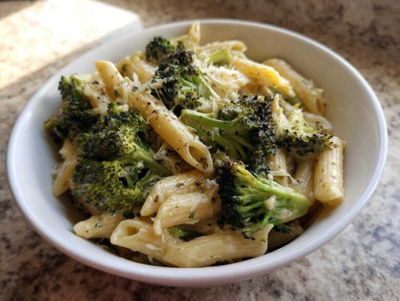 A close-up of creamy broccoli pasta featuring penne noodles, bright green broccoli florets, and grated cheese.