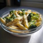 A close-up of creamy broccoli pasta featuring penne noodles, bright green broccoli florets, and grated cheese.