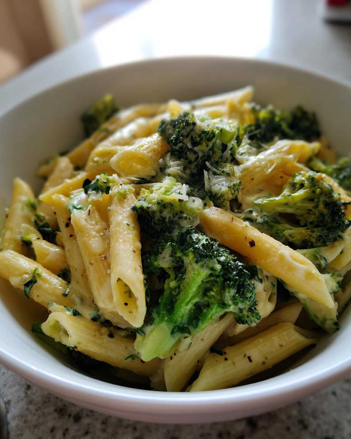 A close-up view of creamy broccoli pasta featuring penne noodles coated in a light sauce with vibrant green broccoli florets.
