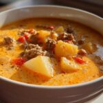 Close-up of a hearty bowl of creamy, orange-hued cheeseburger soup filled with ground beef and potato chunks.