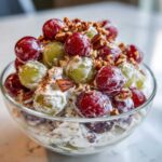 Close-up of a glass bowl filled with creamy chicken salad chick grape salad topped with pecans.