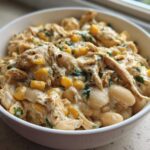Close-up of a white bowl filled with creamy crockpot white chicken chili, featuring shredded chicken, white beans, and corn.