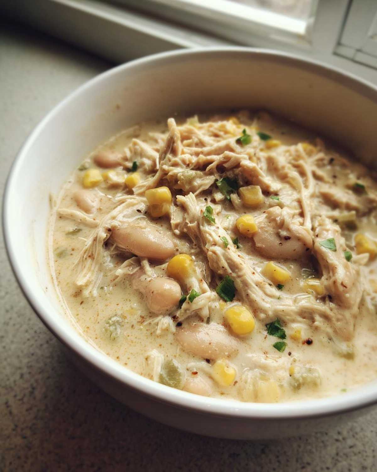 Close-up of a bowl filled with creamy crockpot white chicken chili, featuring shredded chicken, white beans, and corn.