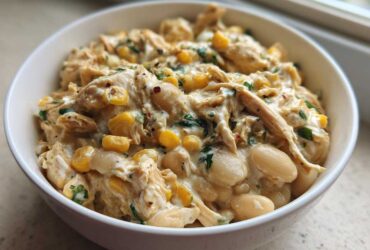 Close-up of a white bowl filled with creamy crockpot white chicken chili, featuring shredded chicken, white beans, and corn.