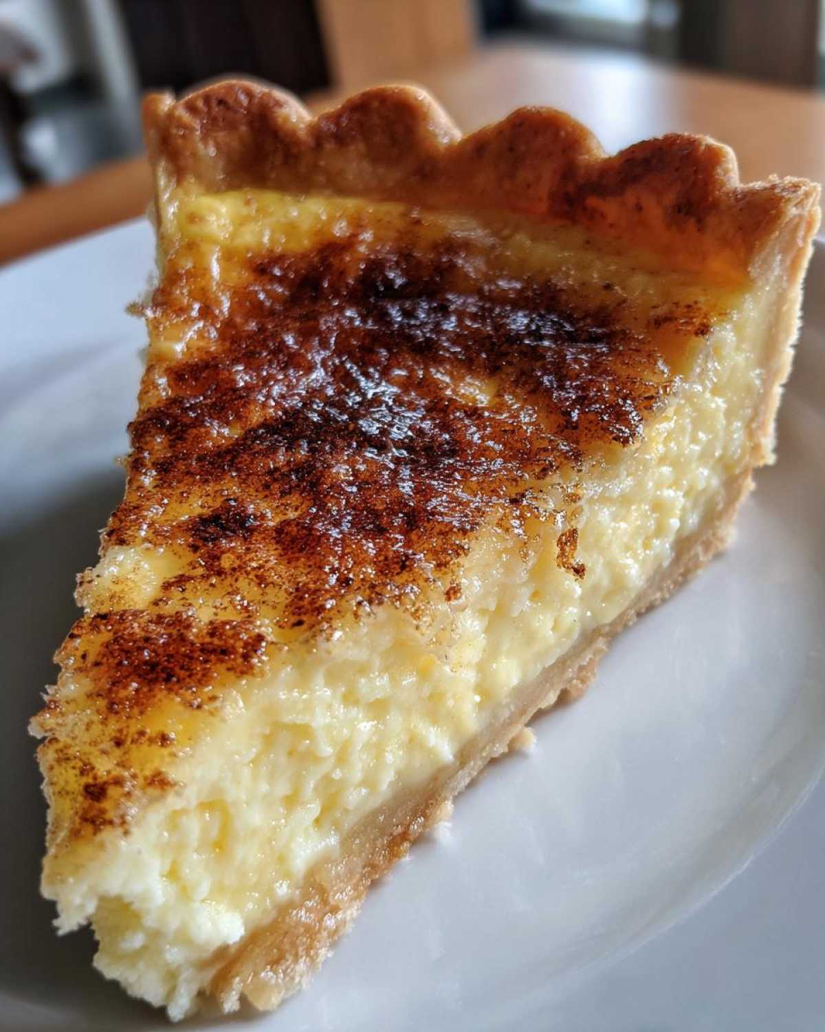 Close-up of a rich slice of egg custard tart with a golden, caramelized top dusted with cinnamon.