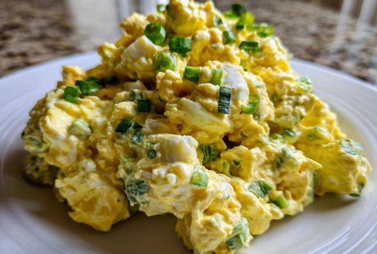 A generous scoop of creamy egg salad recipe garnished with fresh chopped green onions on a white plate.