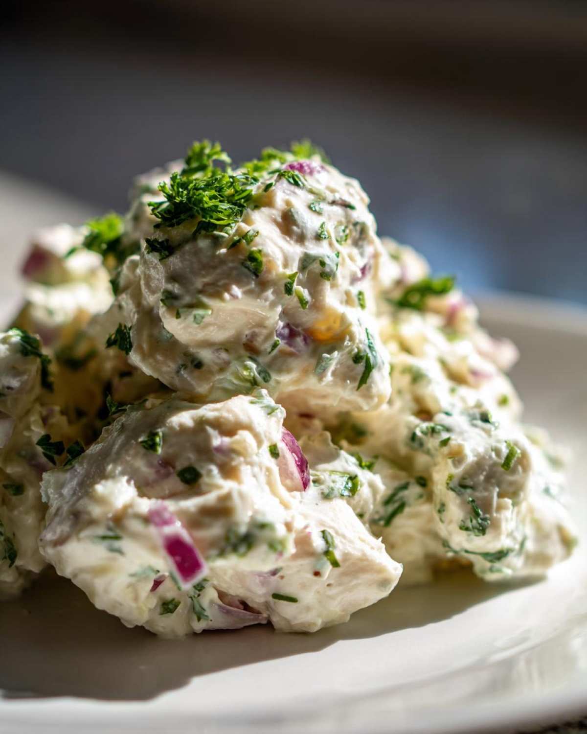 A close-up of creamy greek yogurt chicken salad mixed with red onion and fresh parsley.