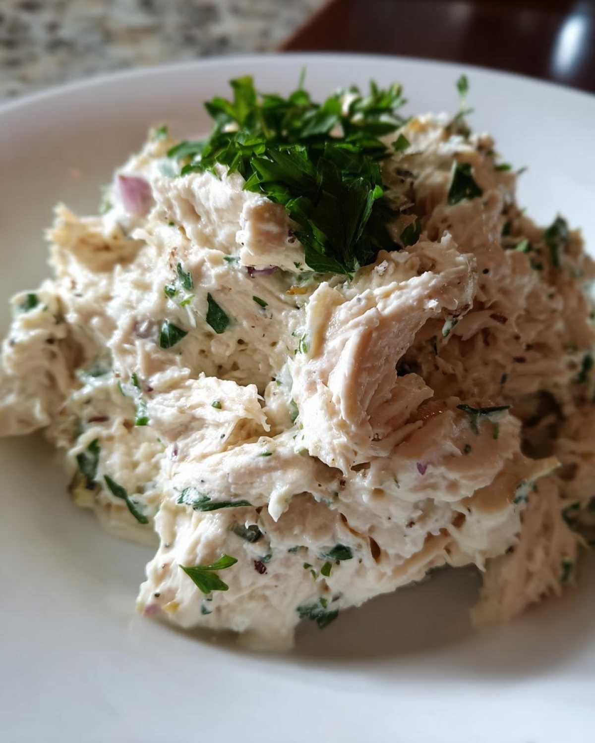A close-up shot of creamy greek yogurt chicken salad mixed with herbs and topped with fresh parsley.