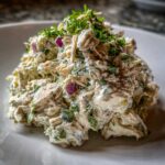 Close-up of a scoop of creamy greek yogurt chicken salad mixed with red onion and topped with fresh parsley.