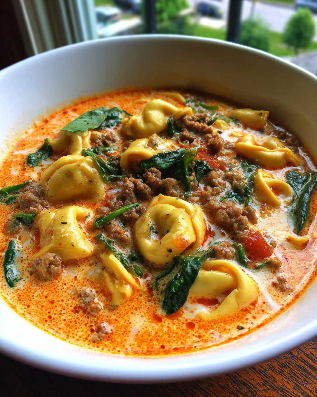 Close-up of creamy italian sausage tortellini soup with spinach in a white bowl.