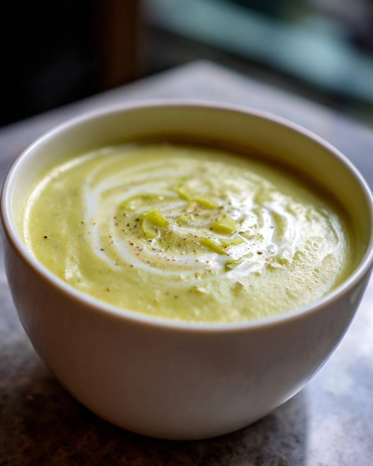 Close-up of a bowl of creamy green leek soup, garnished with a swirl of cream and cracked pepper.
