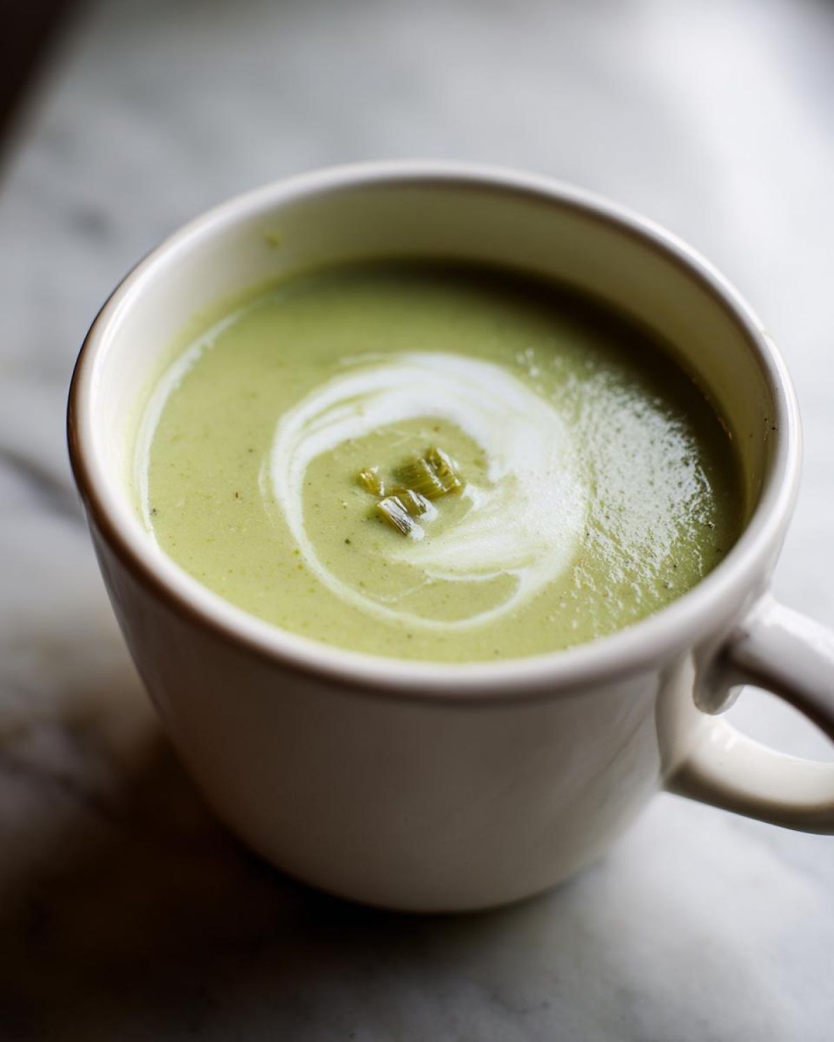 Close-up of a creamy green leek soup garnished with a swirl of cream and chopped leeks.