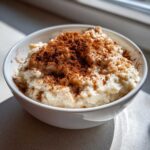 A close-up of creamy rice pudding served in a white bowl, generously topped with ground cinnamon.