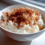Close-up of creamy rice pudding served in a white bowl, generously topped with ground cinnamon.