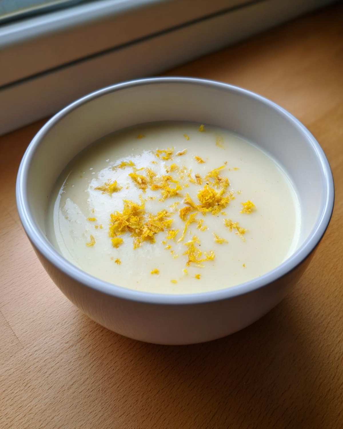 A white bowl filled with creamy roasted cauliflower soup, topped with bright yellow lemon zest.