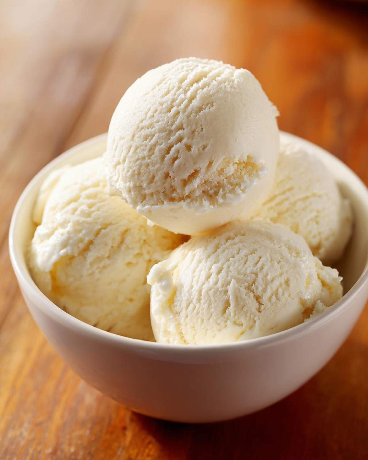 Close-up of several scoops of creamy vanilla protein ice cream in a white bowl on a wooden surface.