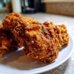 Two pieces of golden brown, extra crispy fried chicken resting on a white plate.