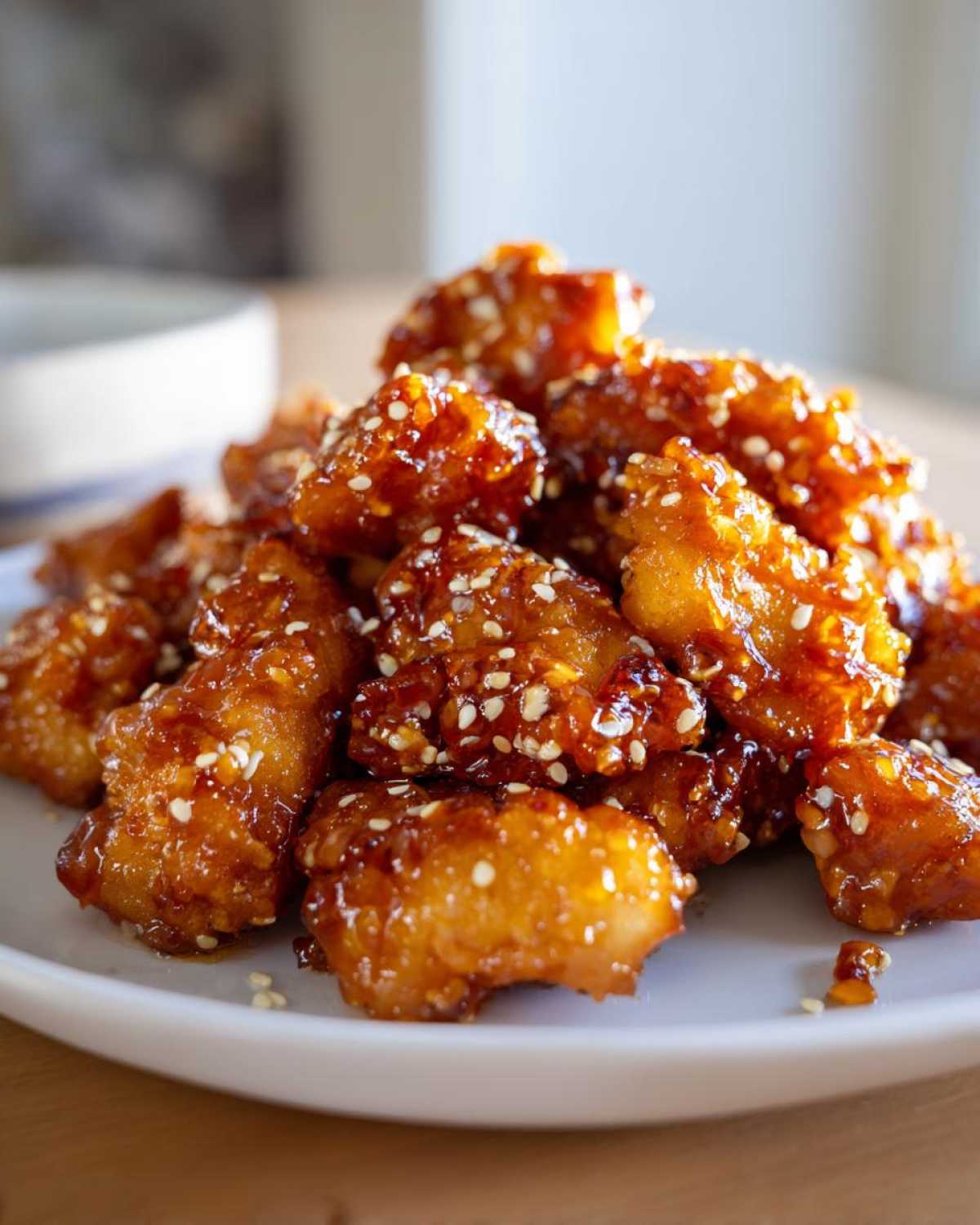 Close-up of crispy, glazed pieces of orange chicken recipe topped generously with white sesame seeds.