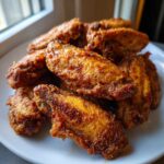 A close-up of a pile of perfectly cooked, seasoned chicken wings on a white plate.