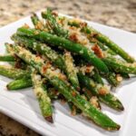 A close-up of bright green beans topped with crispy, golden breadcrumbs served on a white plate.