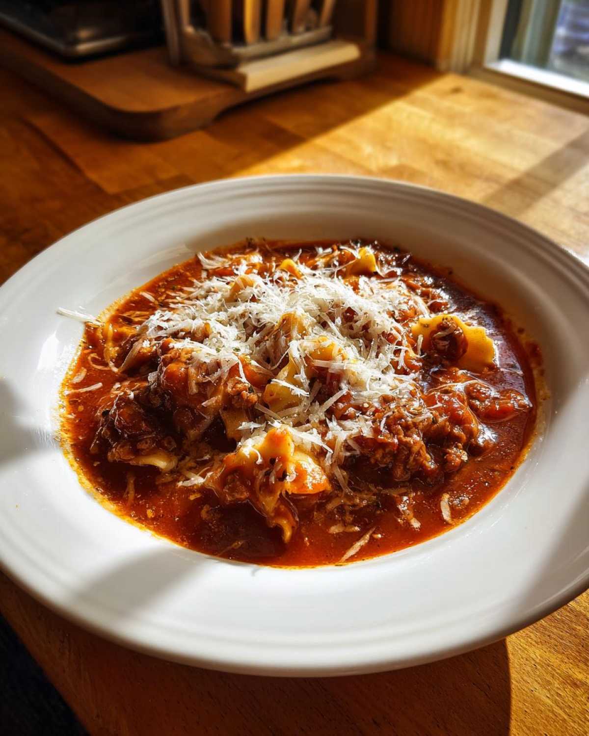 A white bowl filled with rich crockpot lasagna soup topped generously with shredded Parmesan cheese.