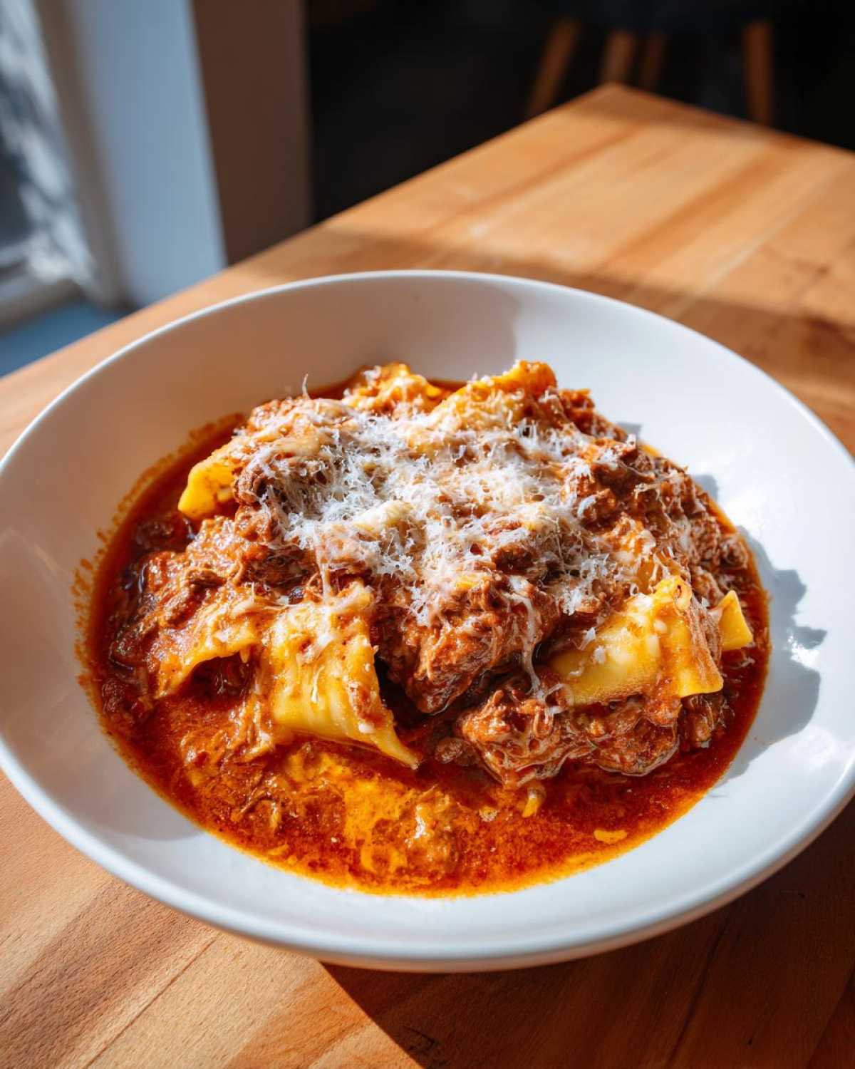 A white bowl filled with rich crockpot lasagna soup, featuring pasta, meat sauce, and topped with grated Parmesan cheese.