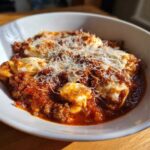 A white bowl filled with rich crockpot lasagna soup featuring meat sauce, pasta, and melted mozzarella topped with grated Parmesan cheese.