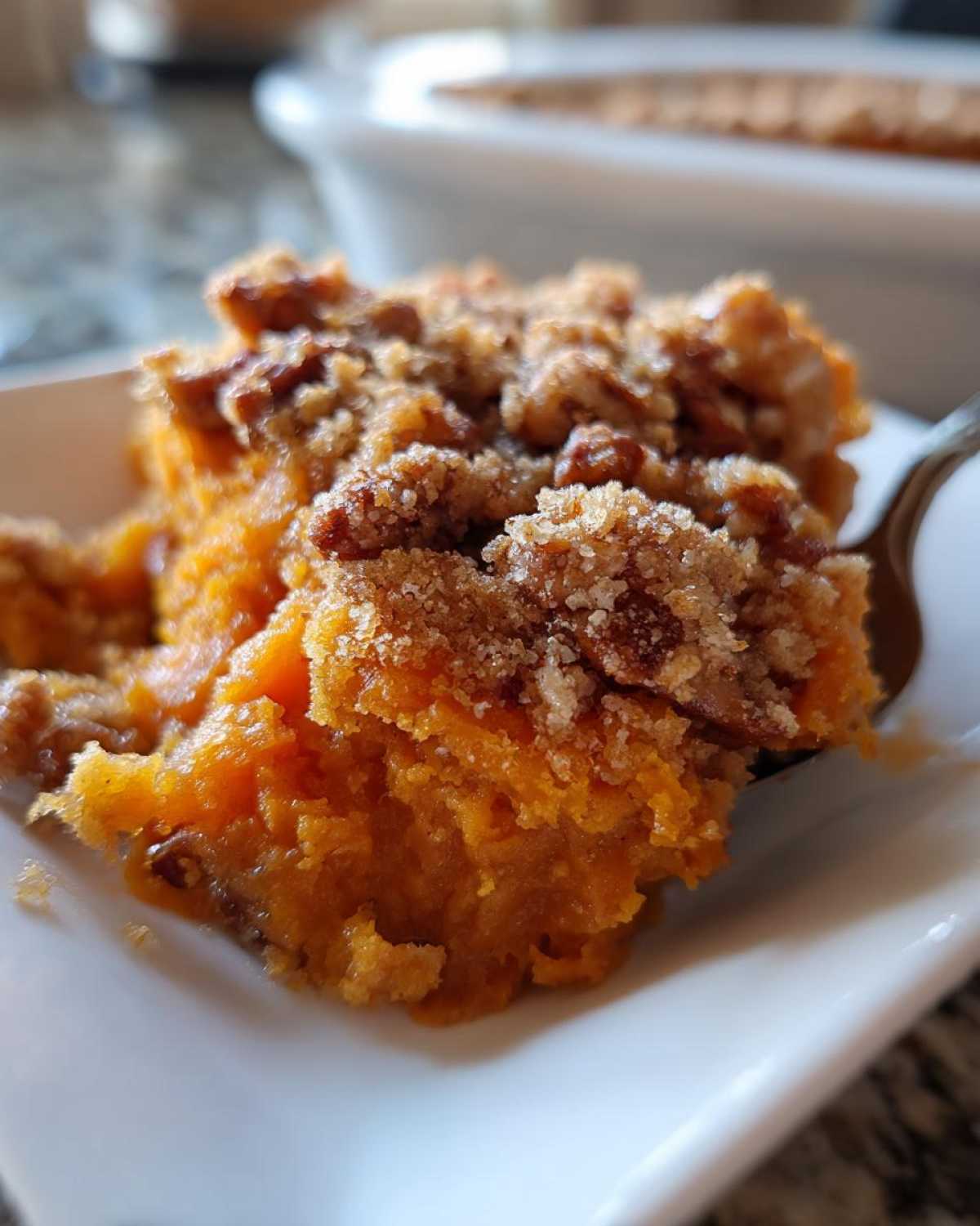 Close-up of a spoonful of rich, orange crockpot sweet potato casserole topped with a brown sugar and pecan crumble.
