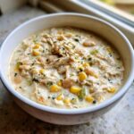 A close-up of a hearty bowl of creamy crockpot white chicken chili with shredded chicken, white beans, and corn.