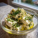 Close-up of cubed marinated cheese soaking in olive oil and topped generously with fresh chopped chives.