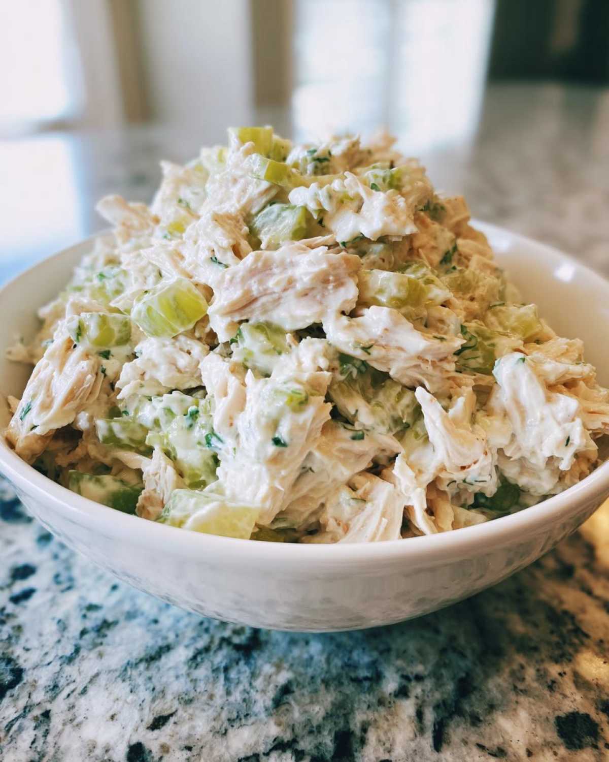 Close-up of a white bowl filled high with creamy dill pickle chicken salad featuring shredded chicken and celery chunks.
