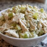 A close-up view of creamy dill pickle chicken salad featuring shredded chicken and green pickle chunks in a white bowl.