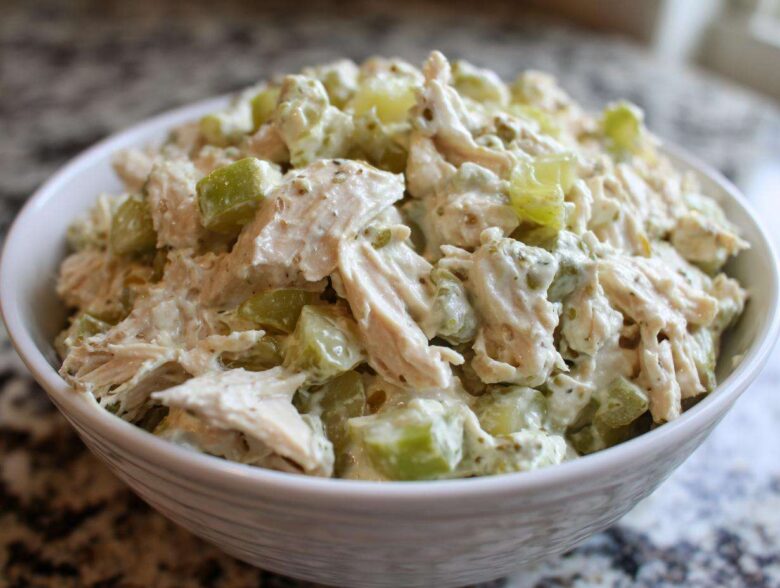 A close-up view of creamy dill pickle chicken salad featuring shredded chicken and green pickle chunks in a white bowl.