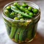 Close-up of fresh green beans and dill being pickled in a glass jar to make dilly beans.