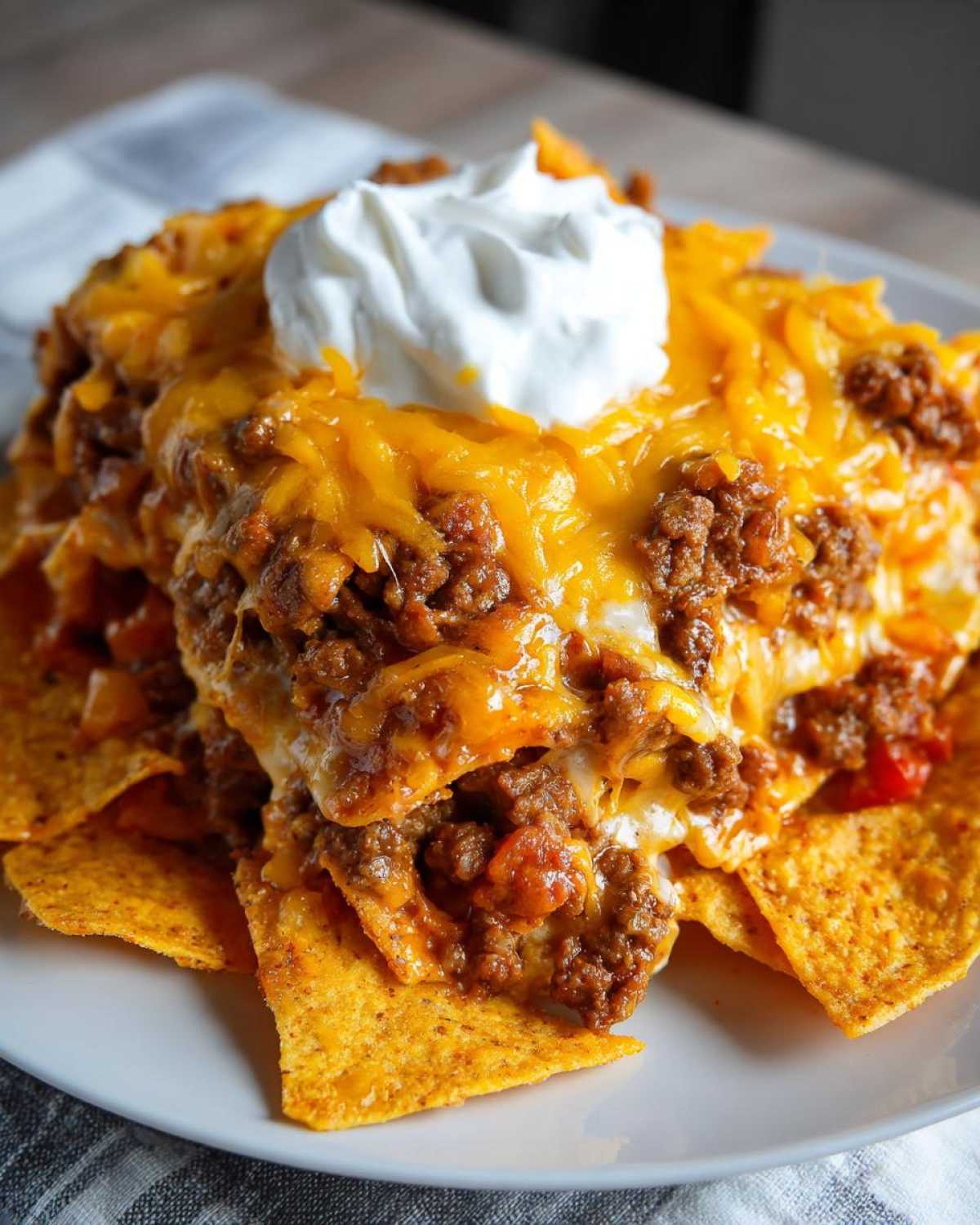 Close-up of a serving of Dorito Casserole topped with melted cheddar cheese, seasoned ground beef, and a dollop of sour cream.