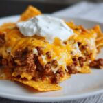 Close-up of a serving of Dorito Casserole topped with melted cheddar cheese and a dollop of sour cream.
