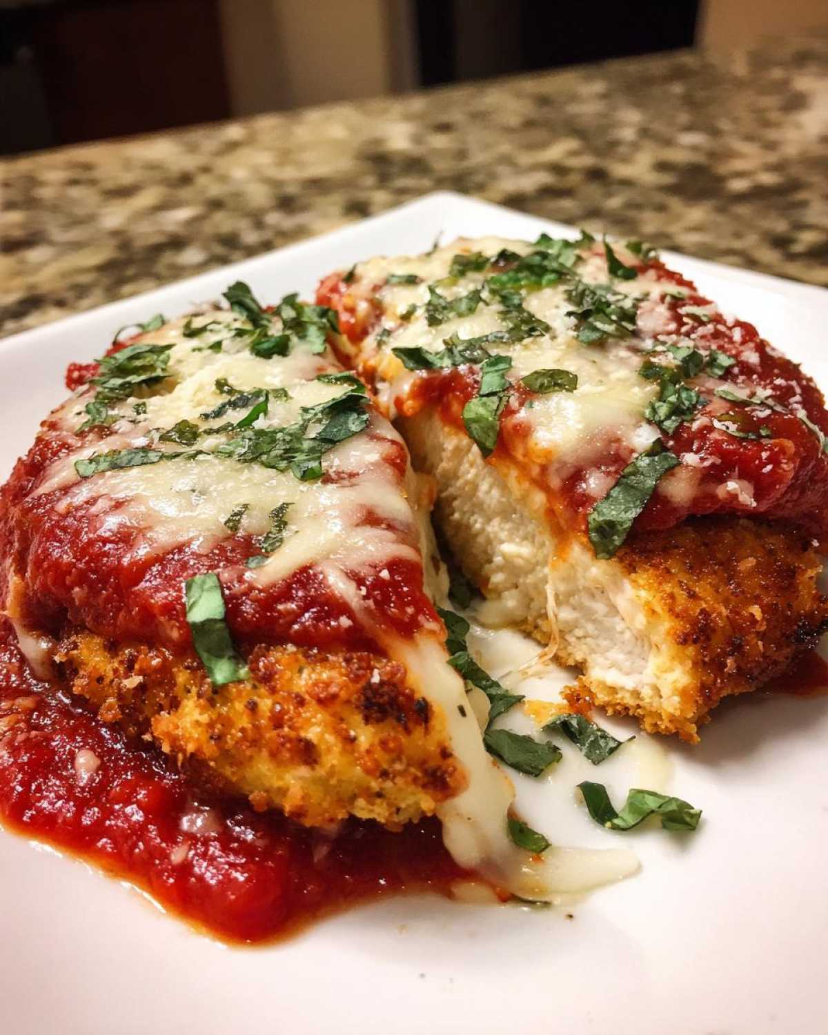Cross-section of Easy Chicken Parmesan showing breaded chicken, melted mozzarella, marinara sauce, and fresh basil.