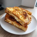 Close-up of stacked, golden brown easy french toast halves filled with cream cheese, served on a white plate.