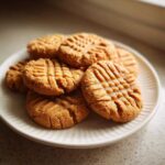 A stack of freshly baked Easy Peanut Butter Cookies showing classic criss-cross fork marks on a white plate.