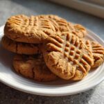 A stack of golden brown Easy Peanut Butter Cookies featuring classic criss-cross fork marks, resting on a white plate.