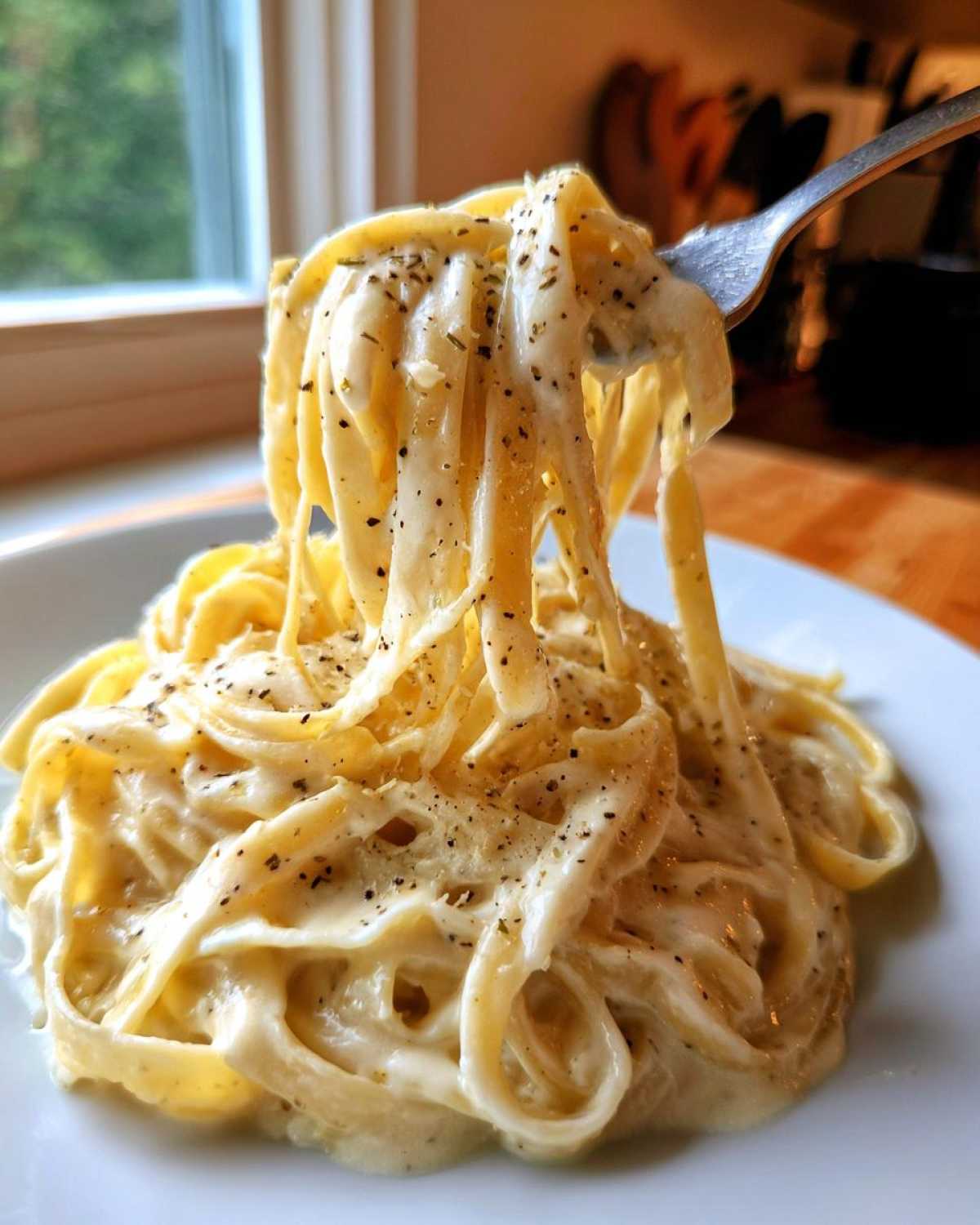 A fork lifts fettuccine coated in rich homemade alfredo sauce, seasoned with black pepper.