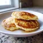 A stack of three fluffy almond flour pancakes drizzled with syrup, served on a white plate.