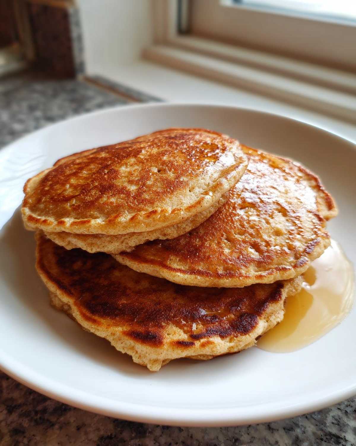 A stack of three golden brown almond flour pancakes drizzled with syrup on a white plate.