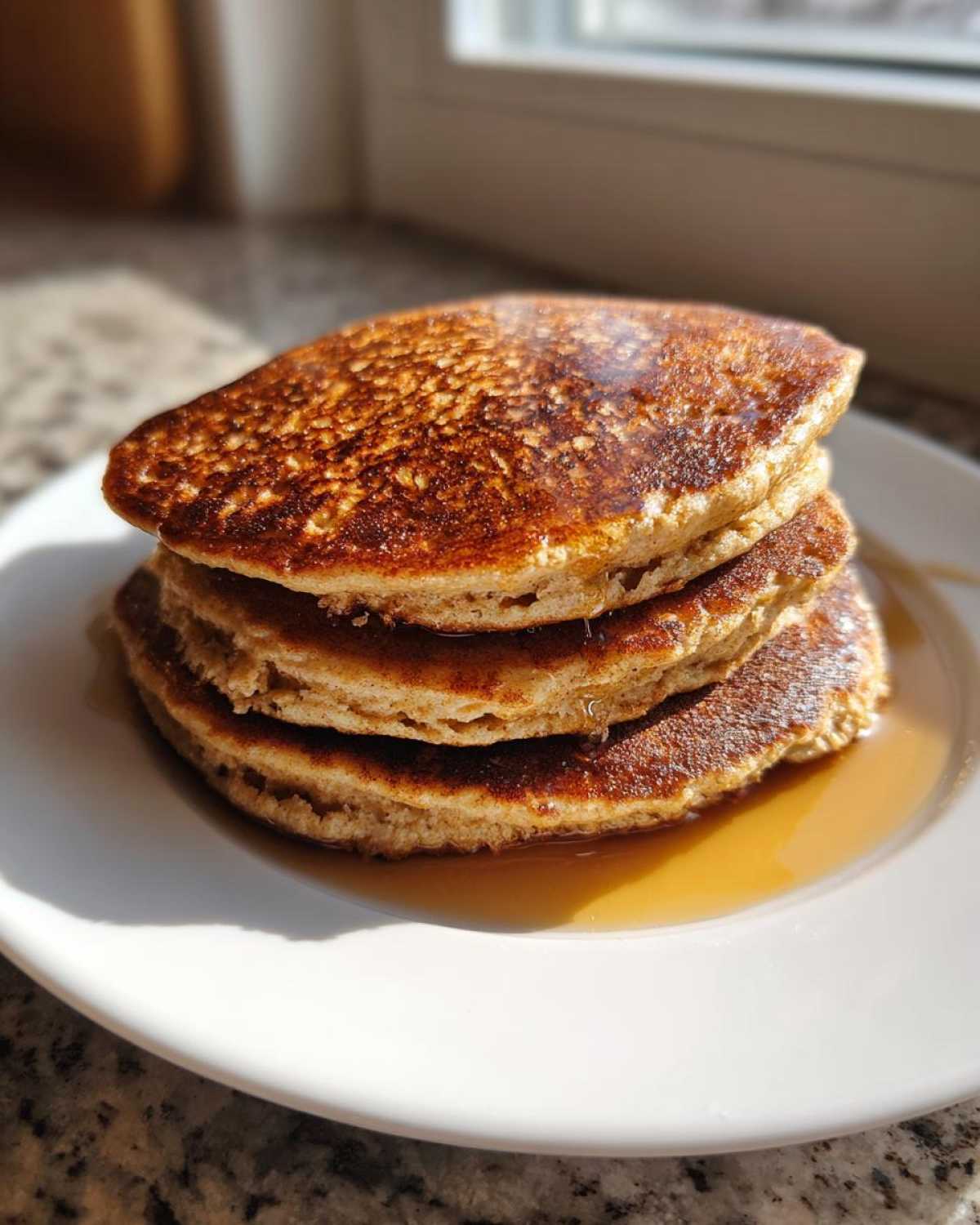 A stack of four fluffy almond flour pancakes drizzled with maple syrup on a white plate.