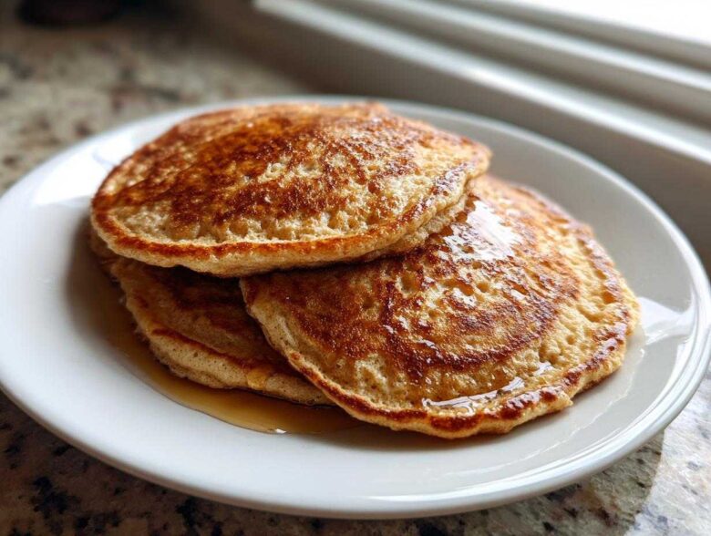 A stack of three golden-brown almond flour pancakes drizzled with syrup on a white plate.