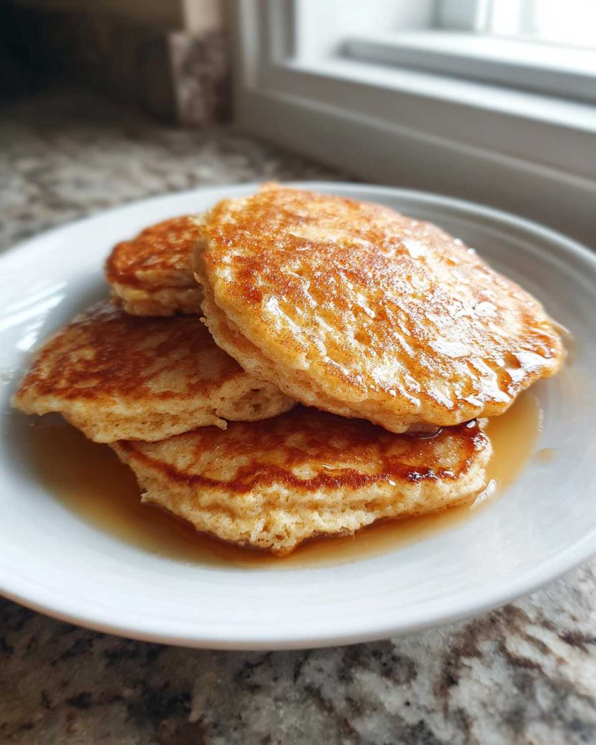 A stack of three fluffy almond flour pancakes drizzled generously with syrup on a white plate.